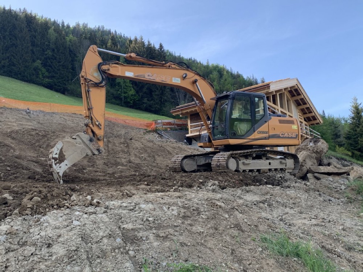 Pelle mécanique en terrassement de terrain en pente devant un chalet à Seyne-les-Alpes